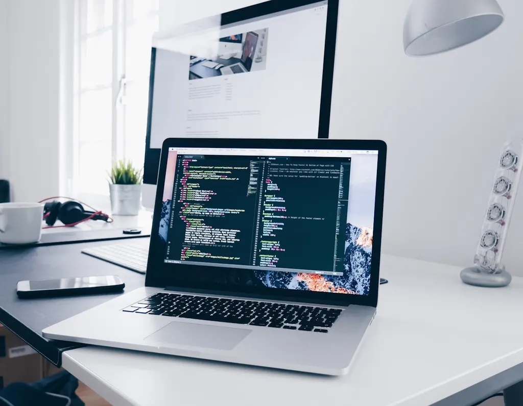 Desk with a laptop showing code, next to a monitor